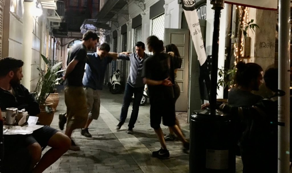 A group of four people dancing under the streetlights in a narrow street.