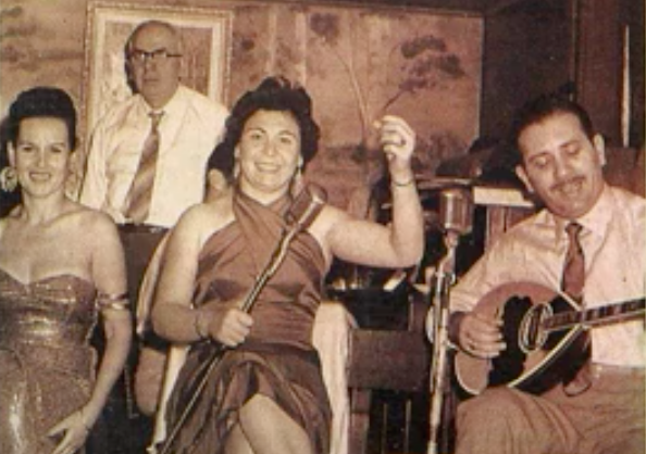 A female singer sitting between a male bouzouki player and a young female.